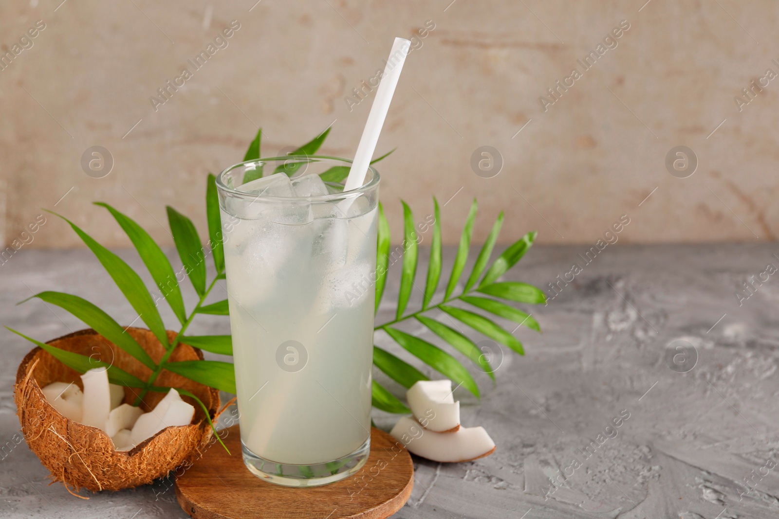 Photo of Glass of coconut water, ice cubes, leaves and nuts on grey table, space for text