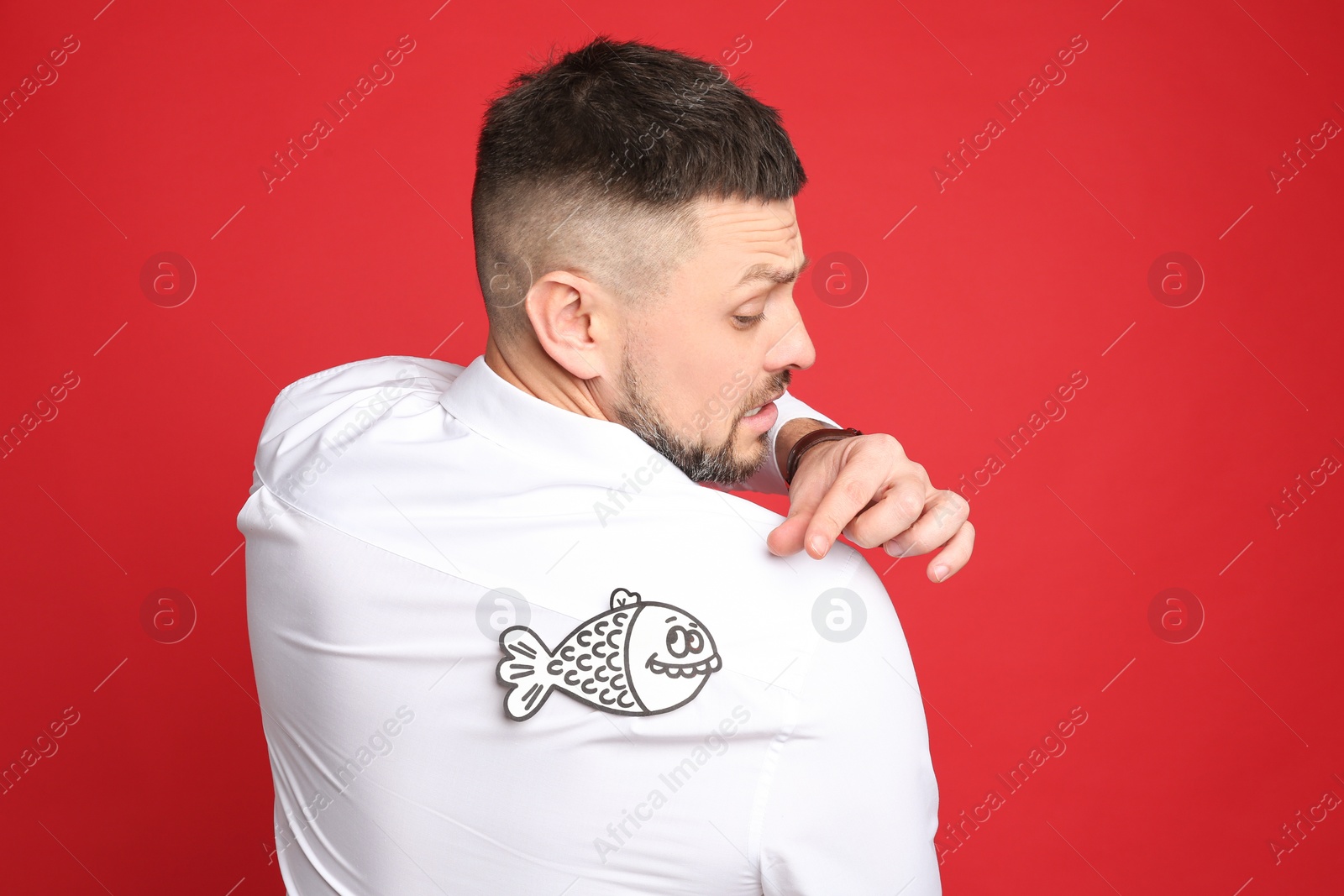 Photo of Man with paper fish on back against red background. April fool's day