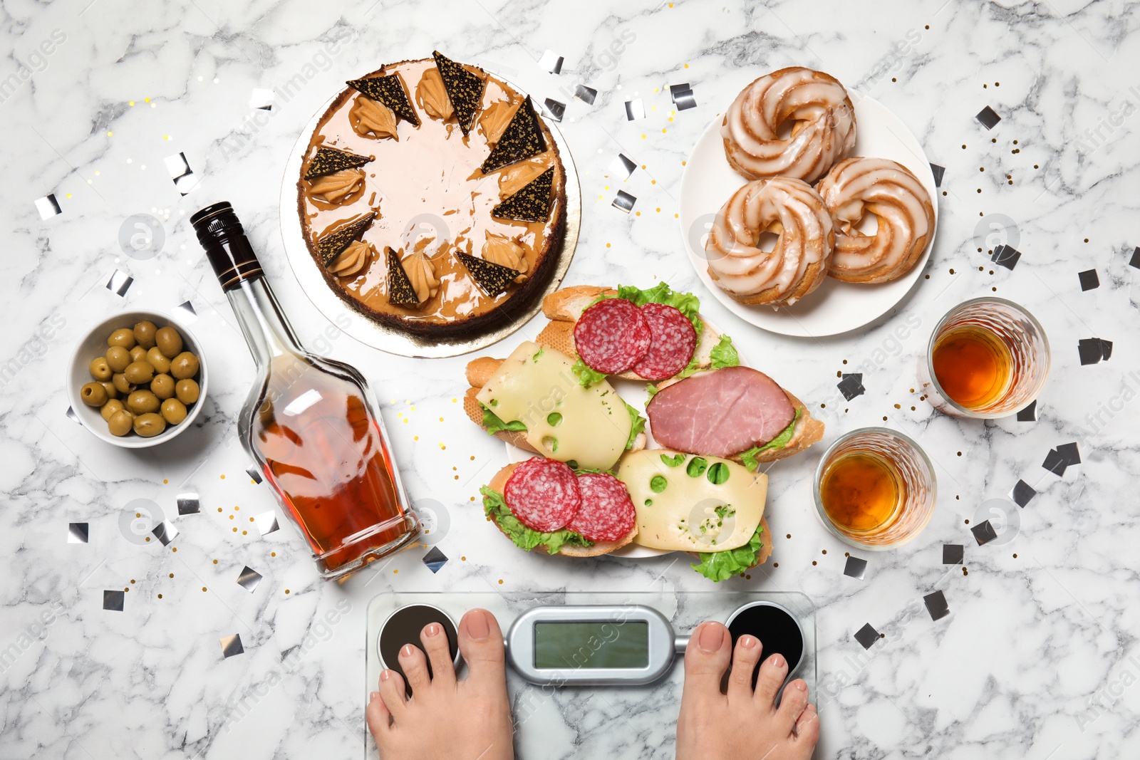Photo of Woman using scale surrounded by food and alcohol after party on floor, top view. Overweight problem