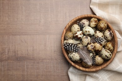 Speckled quail eggs and feathers on wooden table, top view. Space for text