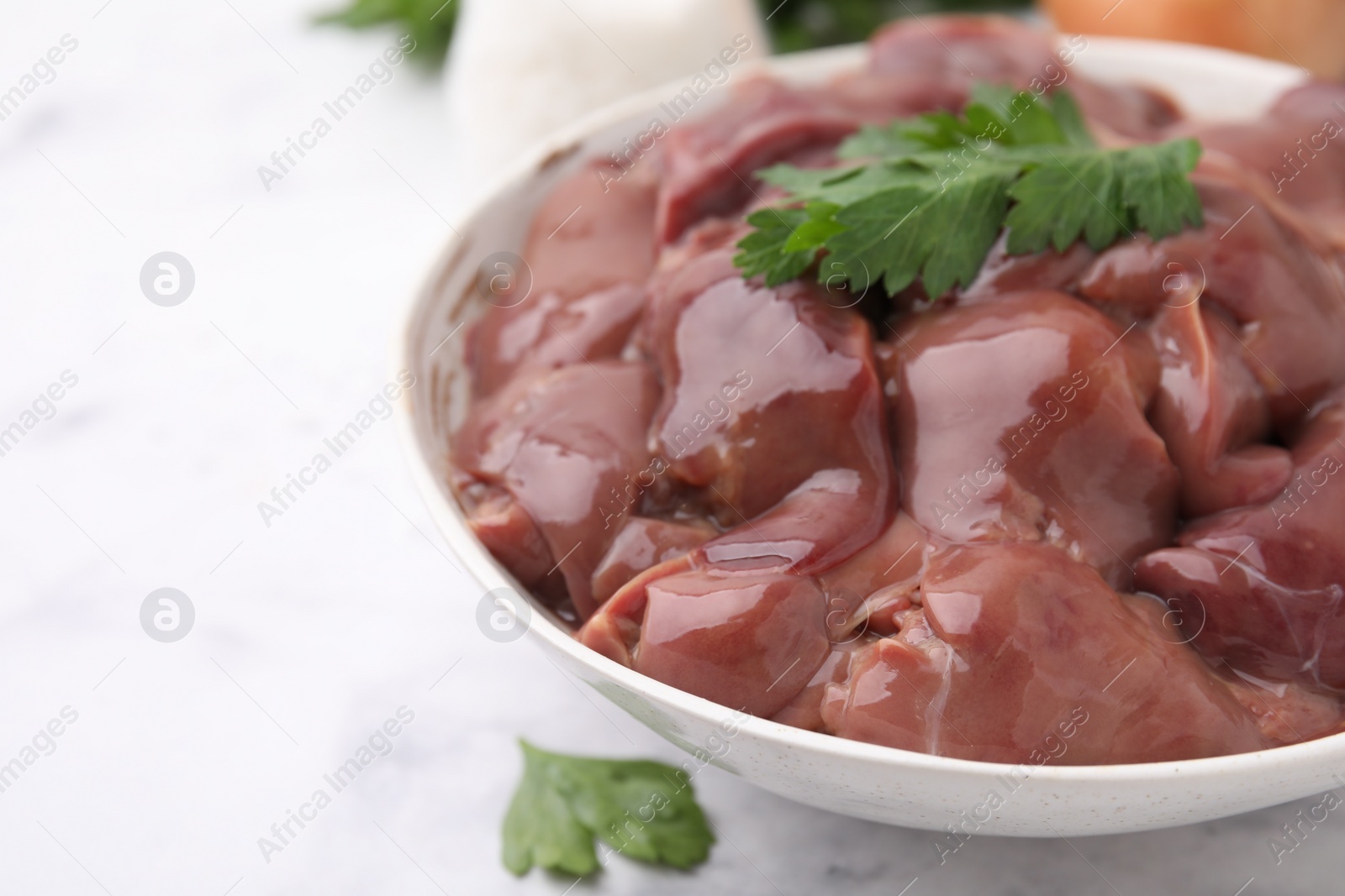 Photo of Bowl of raw chicken liver with parsley on white table, closeup. Space for text