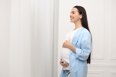 Photo of Happy pregnant woman near window indoors, space for text