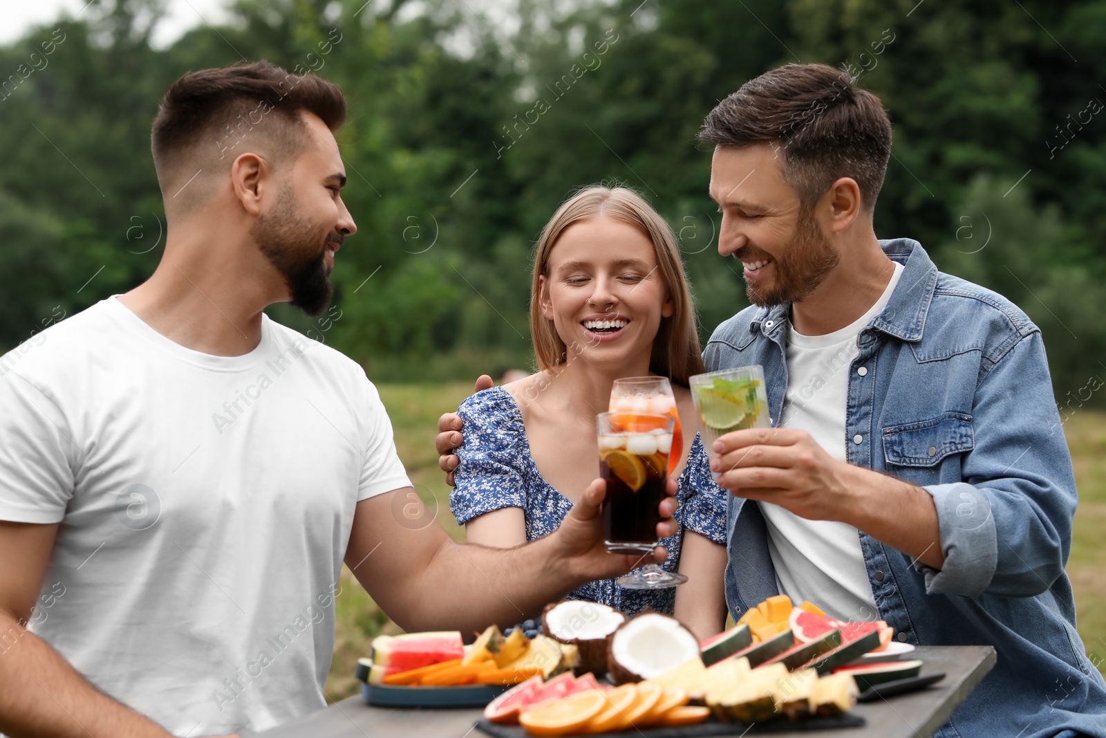 Photo of Happy friends clinking glasses with cocktails at table outdoors