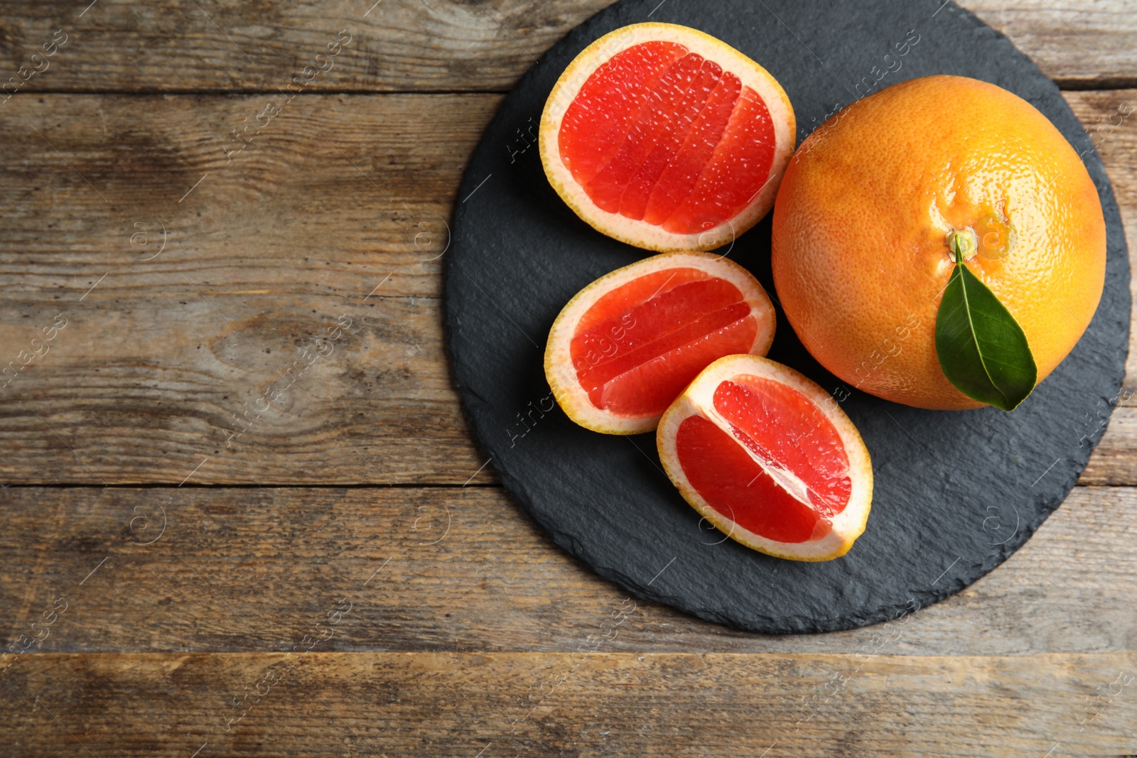 Photo of Slate plate with grapefruits and space for text on wooden background, top view