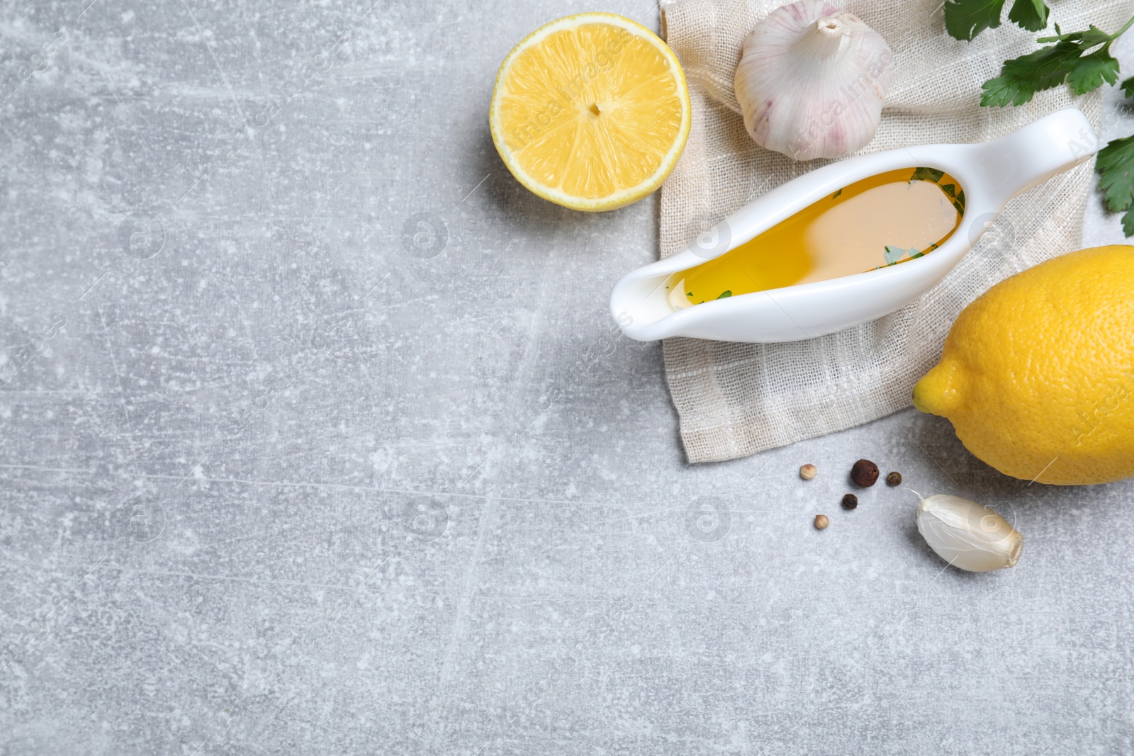 Photo of Ceramic boat of lemon sauce and ingredients on light grey table, flat lay with space for text. Delicious salad dressing