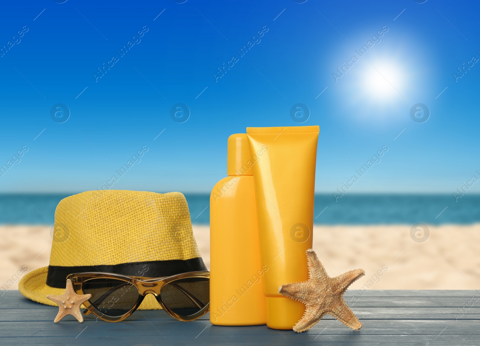 Image of Skin sun protection products and beach accessories on blue wooden table against seascape. Space for design