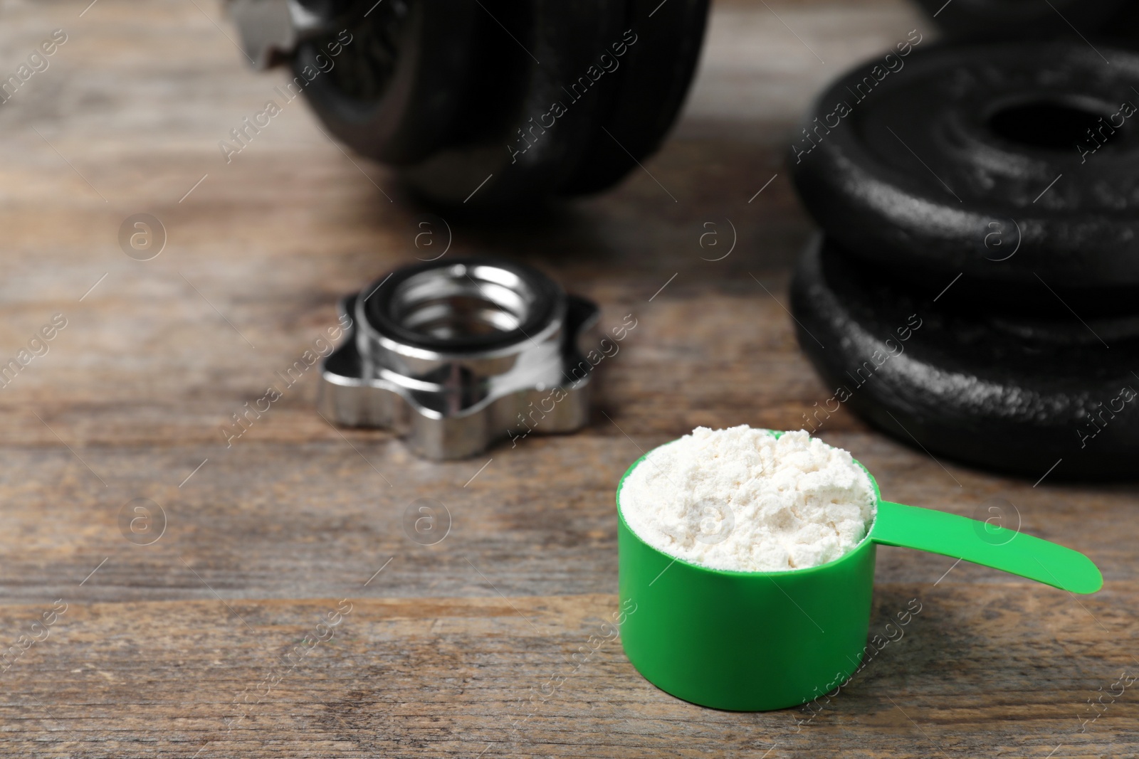 Photo of Scoop with protein powder and dumbbell parts on wooden table. Space for text