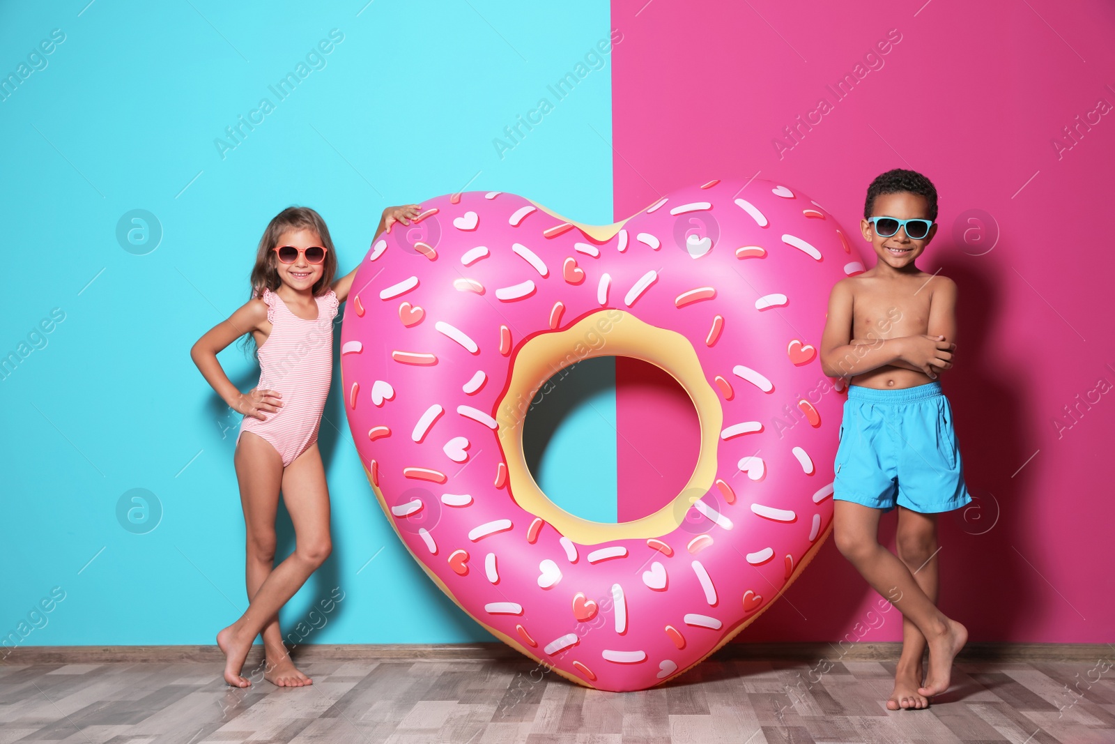 Photo of Cute little children with bright heart shaped inflatable ring near color wall