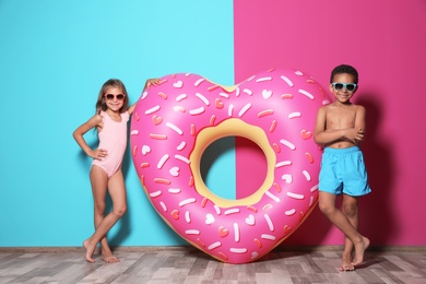 Cute little children with bright heart shaped inflatable ring near color wall