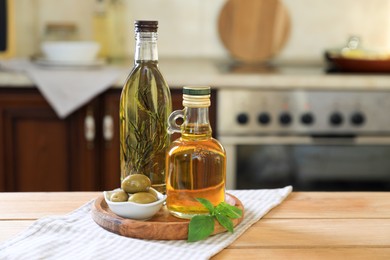 Photo of Different cooking oils, olives and basil on wooden table in kitchen, space for text