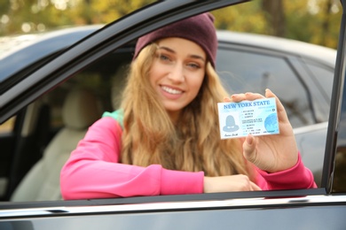 Photo of Young woman holding driving license near open car. Space for text