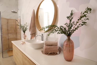 Photo of Vase with beautiful branches and fresh towels near vessel sink in bathroom. Interior design