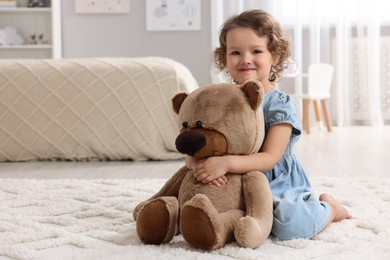 Cute little girl with teddy bear on floor at home