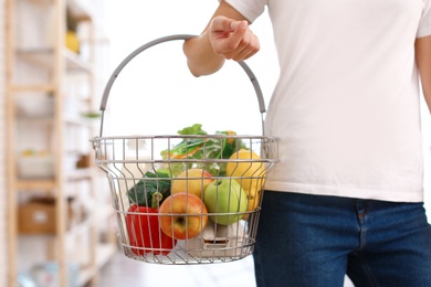 Photo of Woman with shopping basket full of products in grocery store, closeup