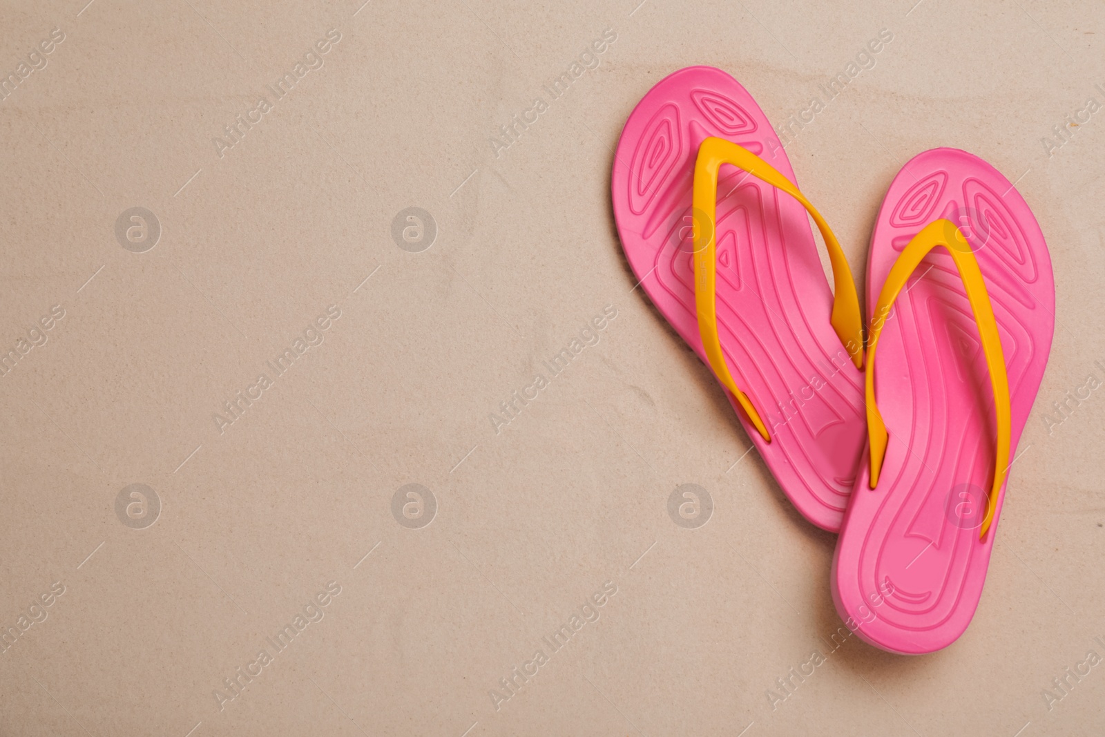 Photo of Pair of pink flip flops on sand, flat lay. Space for text