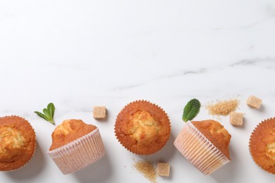 Delicious sweet muffins and brown sugar on white marble table, flat lay. Space for text