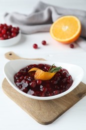 Photo of Fresh cranberry sauce, orange peel and rosemary in bowl on white wooden table, closeup