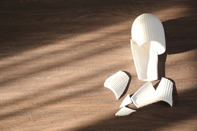 Broken white ceramic vase on wooden floor, flat lay. Space for text