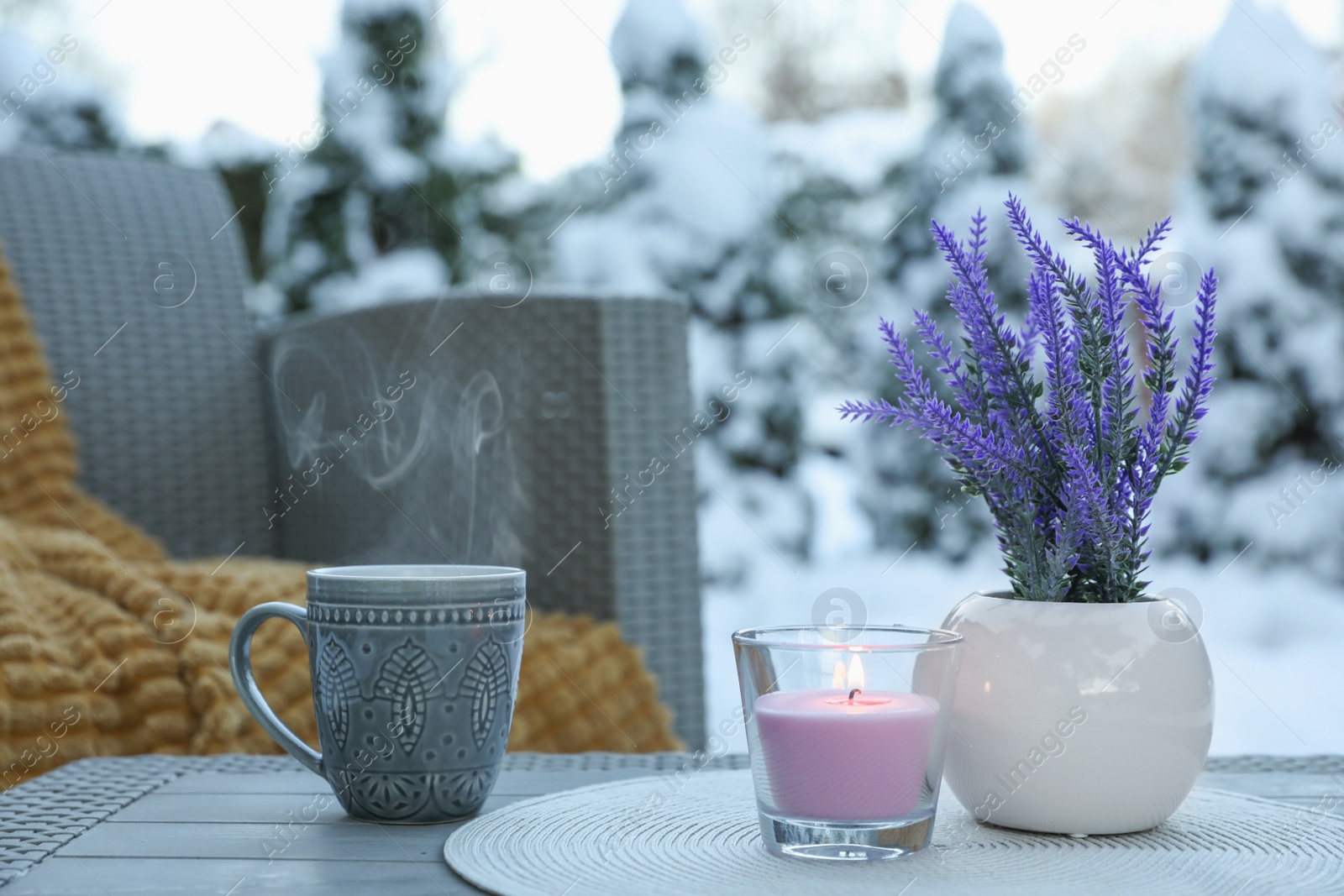 Photo of Burning candle, potted flowers and cup with hot drink on coffee table outdoors. Cosy winter