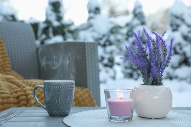 Photo of Burning candle, potted flowers and cup with hot drink on coffee table outdoors. Cosy winter