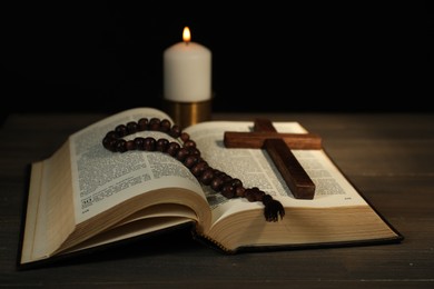 Photo of Church candle, Bible, rosary beads and cross on wooden table, closeup
