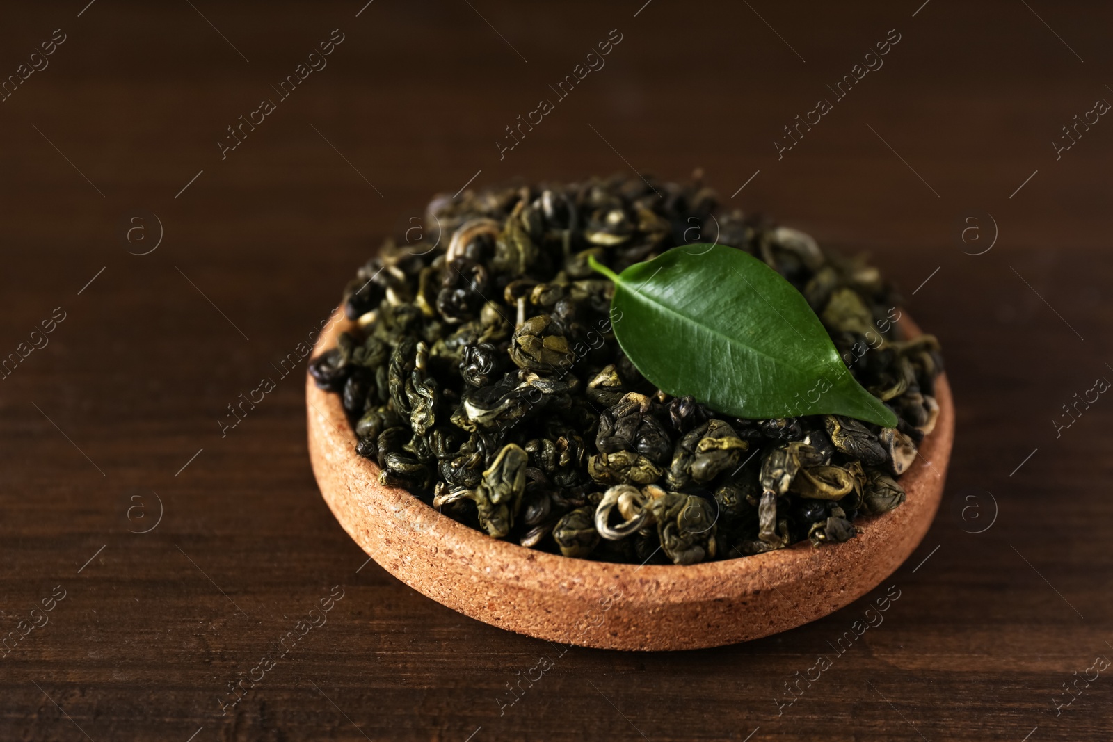 Photo of Dried green tea leaves in cork bowl on wooden table, closeup