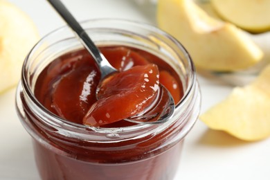 Photo of Taking tasty homemade quince jam from jar at table, closeup