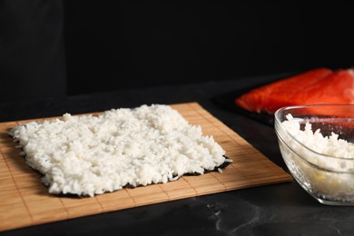 Photo of Cooking process. Unwrapped sushi roll on bamboo mat at dark table, closeup