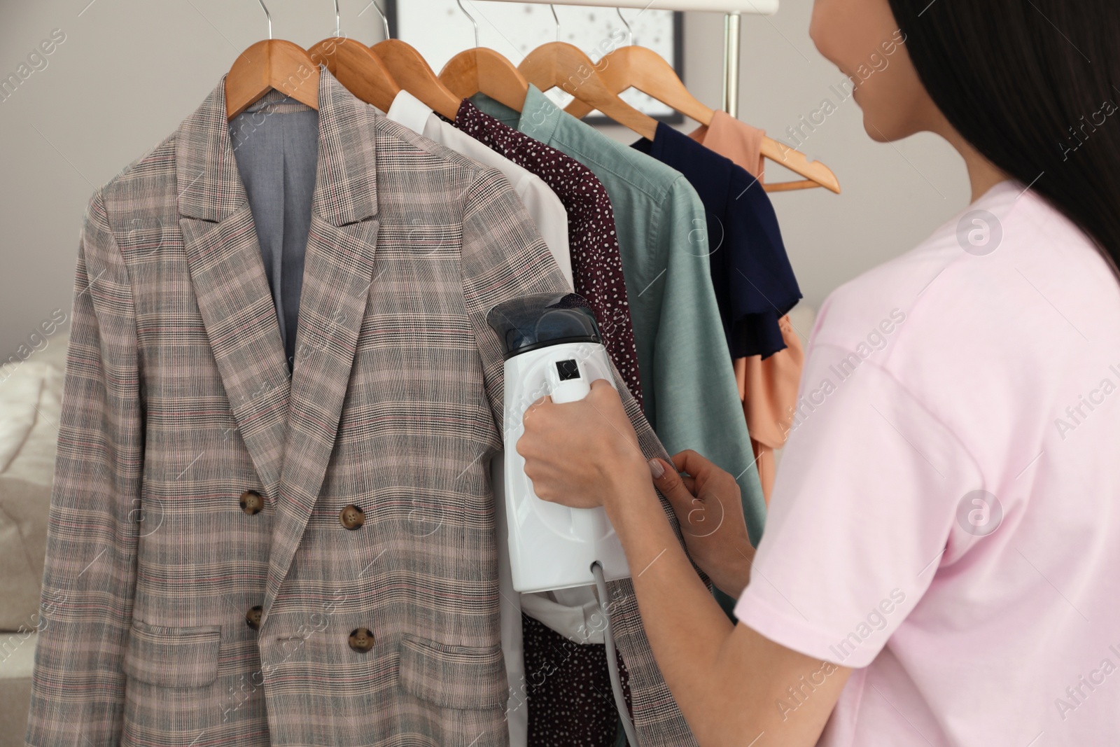 Photo of Woman steaming jacket on hanger at home, closeup