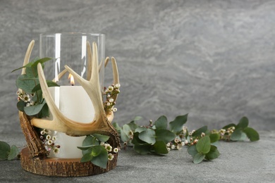 Burning candle in beautiful glass holder and eucalyptus on grey table, space for text