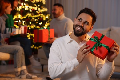 Photo of Christmas celebration in circle of friends. Happy young man with gift box at home, selective focus