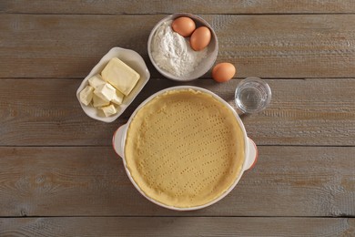 Photo of Making quiche. Baking dish with fresh dough and ingredients on wooden table, flat lay