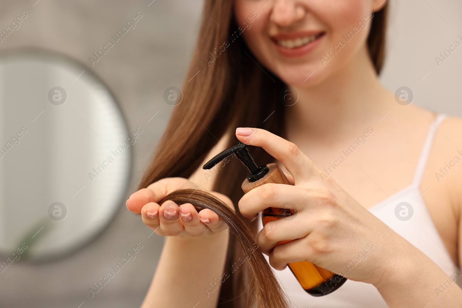 Photo of Woman applying oil hair mask indoors, closeup