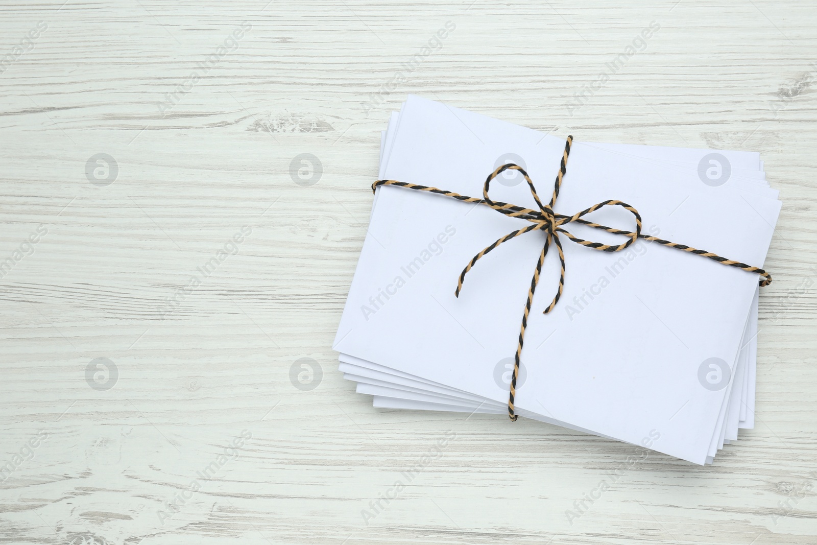 Photo of Stack of letters tied with string on white wooden table, top view. Space for text