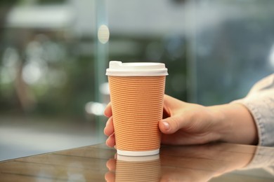 Photo of Woman holding takeaway paper cup at table, closeup. Coffee to go