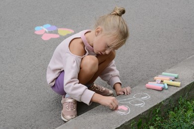 Little child drawing balloons with chalk on asphalt