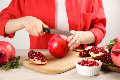 Photo of Woman cutting ripe pomegranate at wooden table, closeup