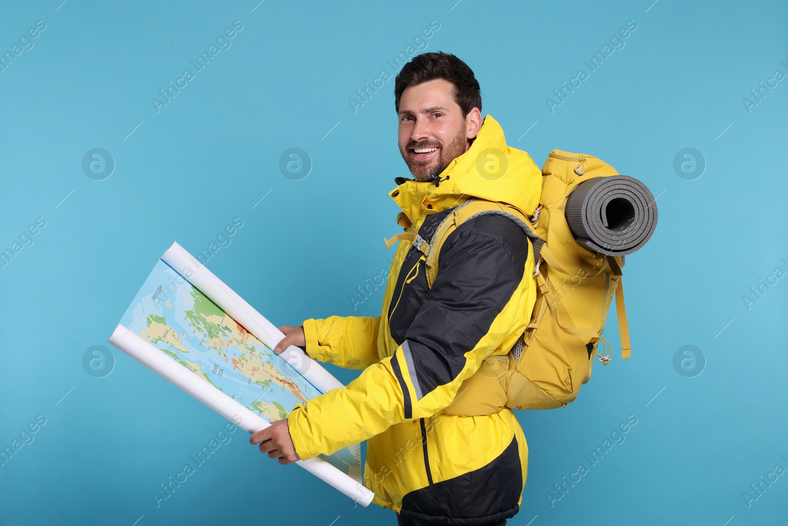 Photo of Happy man with backpack and map on light blue background. Active tourism