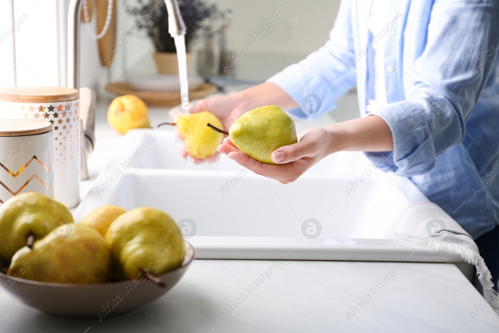 Photo of Woman holding fresh ripe pear in kitchen, closeup