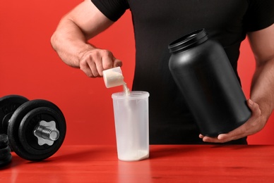 Man preparing protein shake at wooden table against red background, closeup