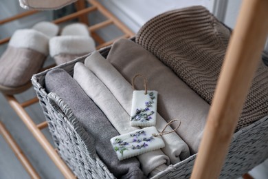 Photo of Beautiful scented wax sachets and folded clothes in wicker basket on rack indoors