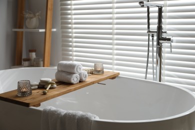 Photo of Wooden tray with spa products and burning candles on bath tub in bathroom