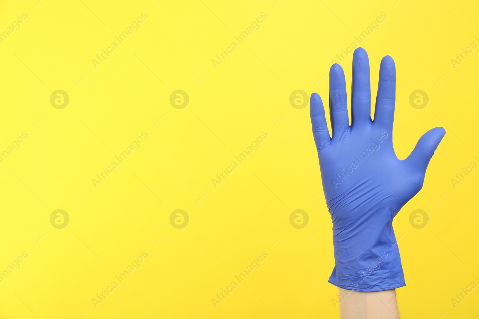Photo of Person in medical gloves on yellow background, closeup of hand. Space for text