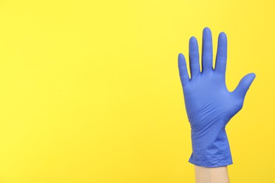 Photo of Person in medical gloves on yellow background, closeup of hand. Space for text