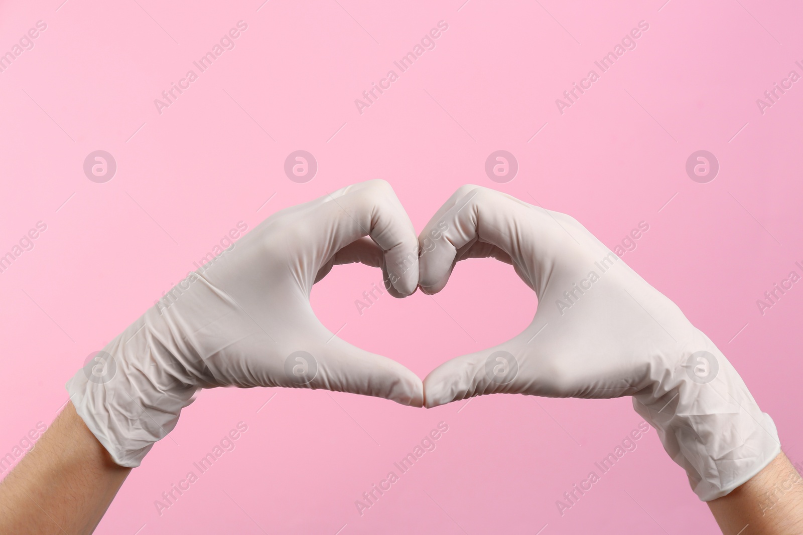 Photo of Person in medical gloves showing heart gesture on pink background, closeup of hands