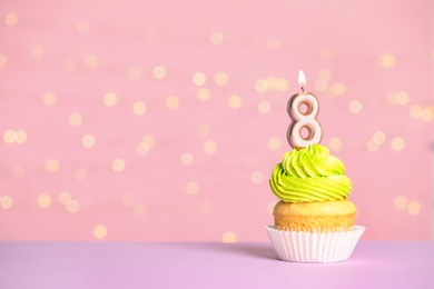 Photo of Birthday cupcake with number eight candle on table against festive lights, space for text