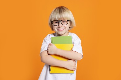 Cute little boy wearing glasses with books on orange background