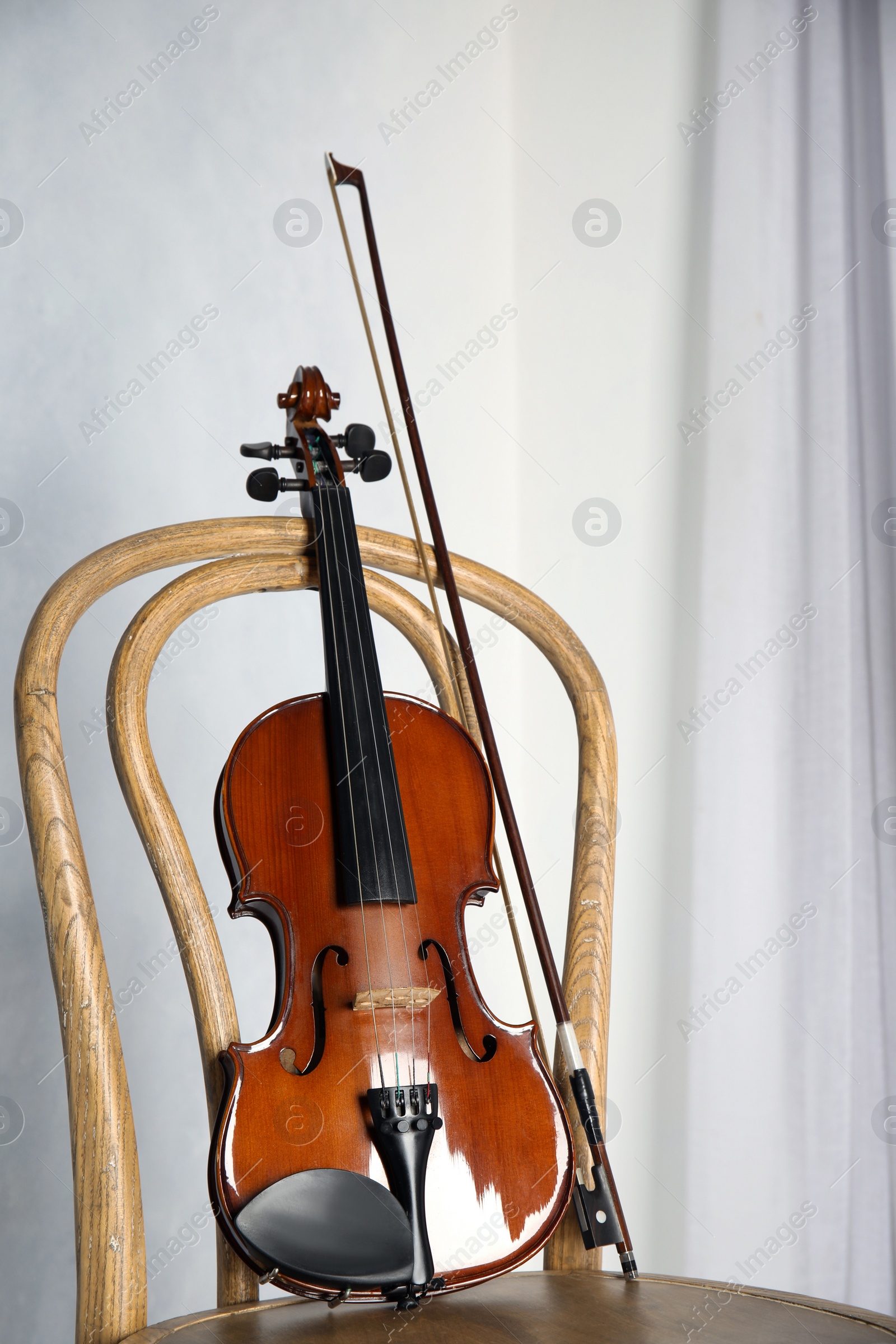 Photo of Classic violin and bow on chair near light wall