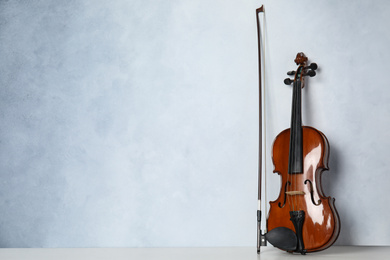 Photo of Beautiful violin and bow on table near light blue wall. Space for text