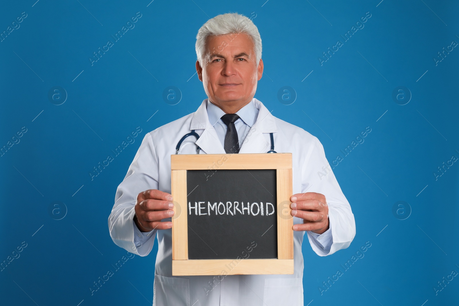 Photo of Doctor holding blackboard with word HEMORRHOID on blue background